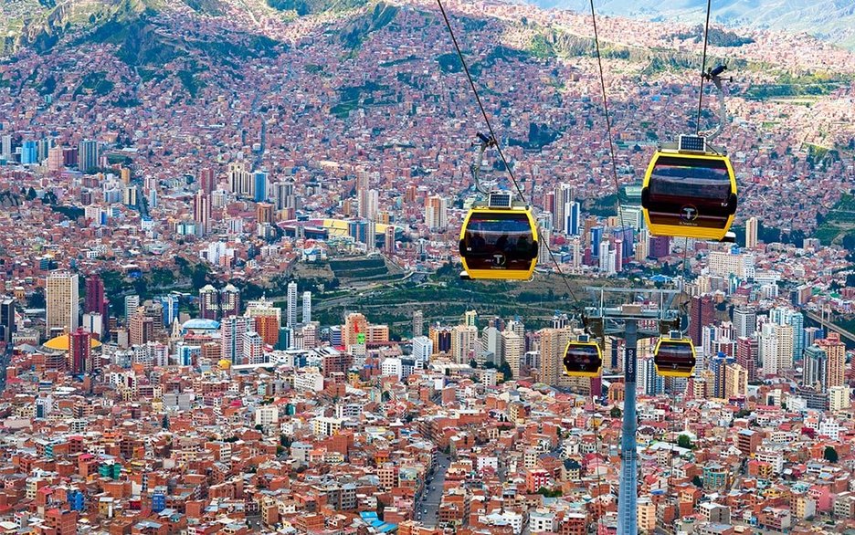 Zu sehen ist eine Seilbahn mit gelben Gondeln und abgedunkelten Scheiben für Berufspendler in Bolivien, die die Millionenstadt La Paz mit der Arbeitervorstadt El Alto verbindet. Link zum Artikel.